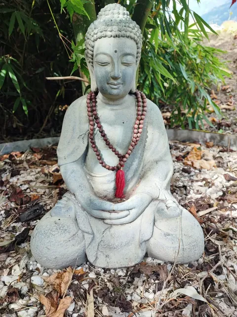 Buddha-Figur mit Mala-Kette im Garten der Praxis